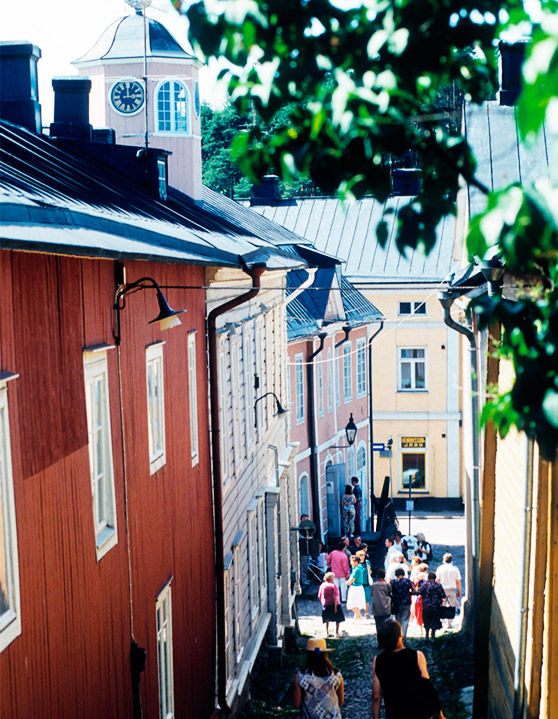 People walking on a cobblestone street between colourful wooden buildings.