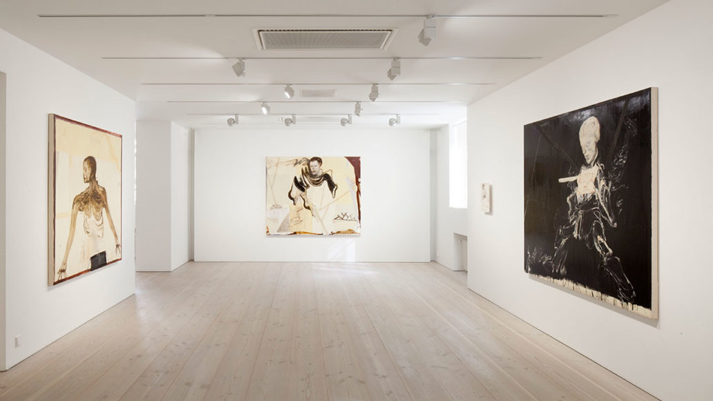 An art gallery with white floors, walls and ceiling and three paintings hanging on the walls. 
