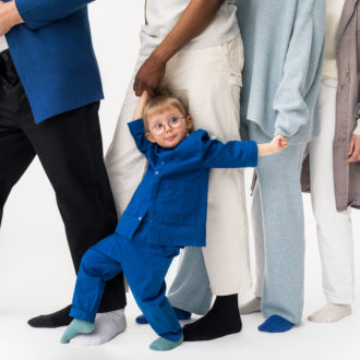 Four people standing in a row with only their legs visible; a smiling young child holding the hands of two of the people.