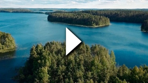 A landscape featuring a lake and some land with forest on. A video play symbol on top.