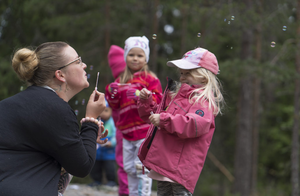 Woman blowing soap bubbles with kindergarden children.