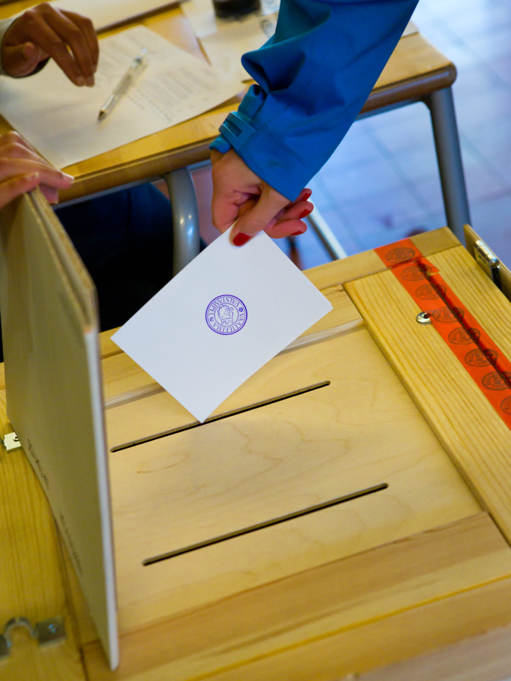 A hand putting a ballot in a box.