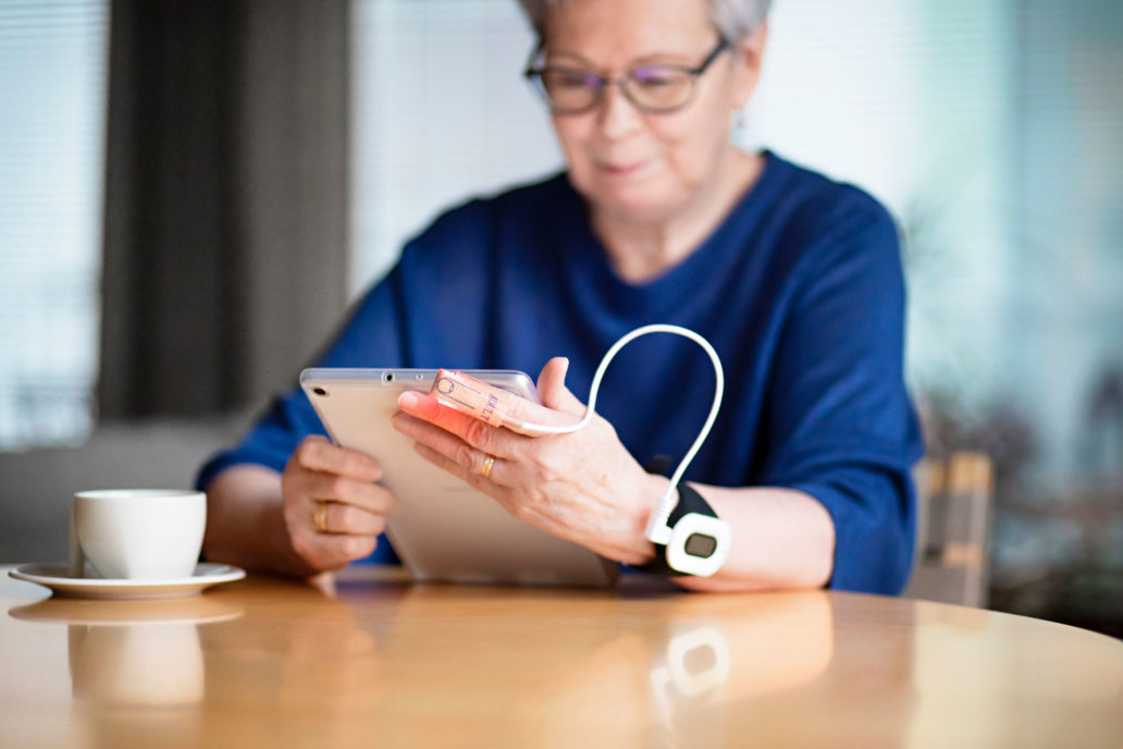 An elderly woman holding a tablet with a health device around her wrist.