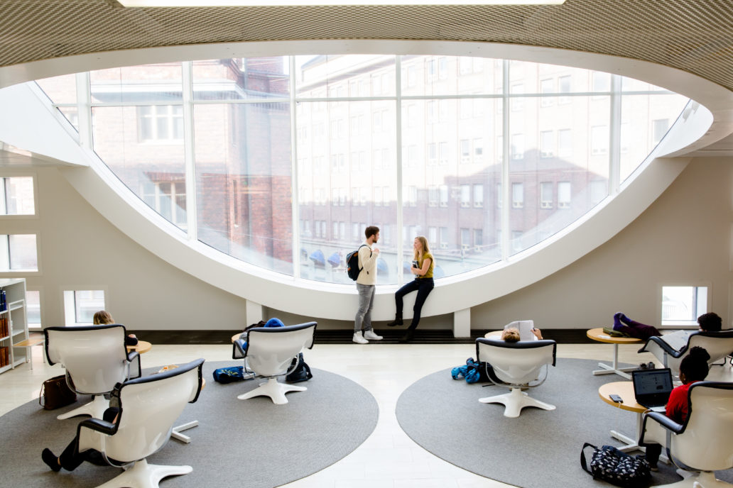 A man and a woman next to big library window talking to each others.