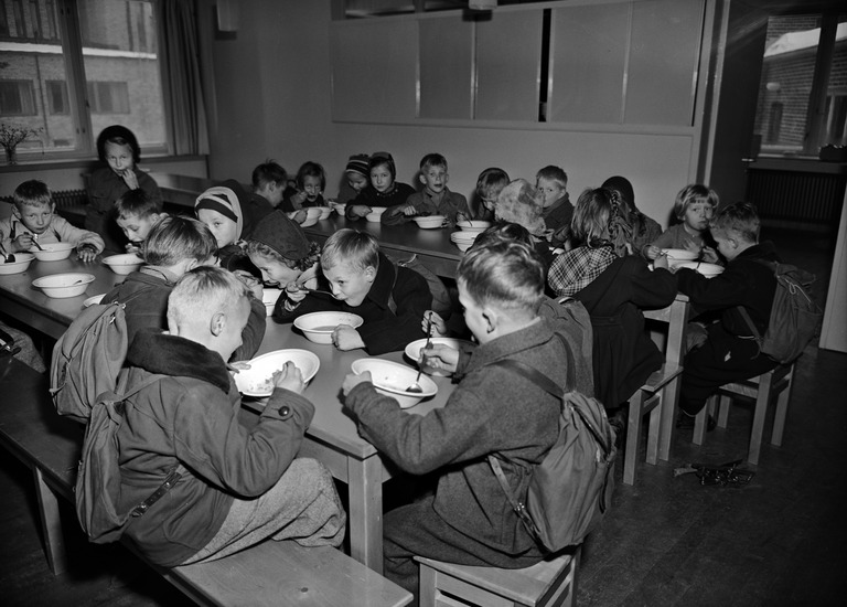 A school cafeteria filled with children eating in the 1950s.