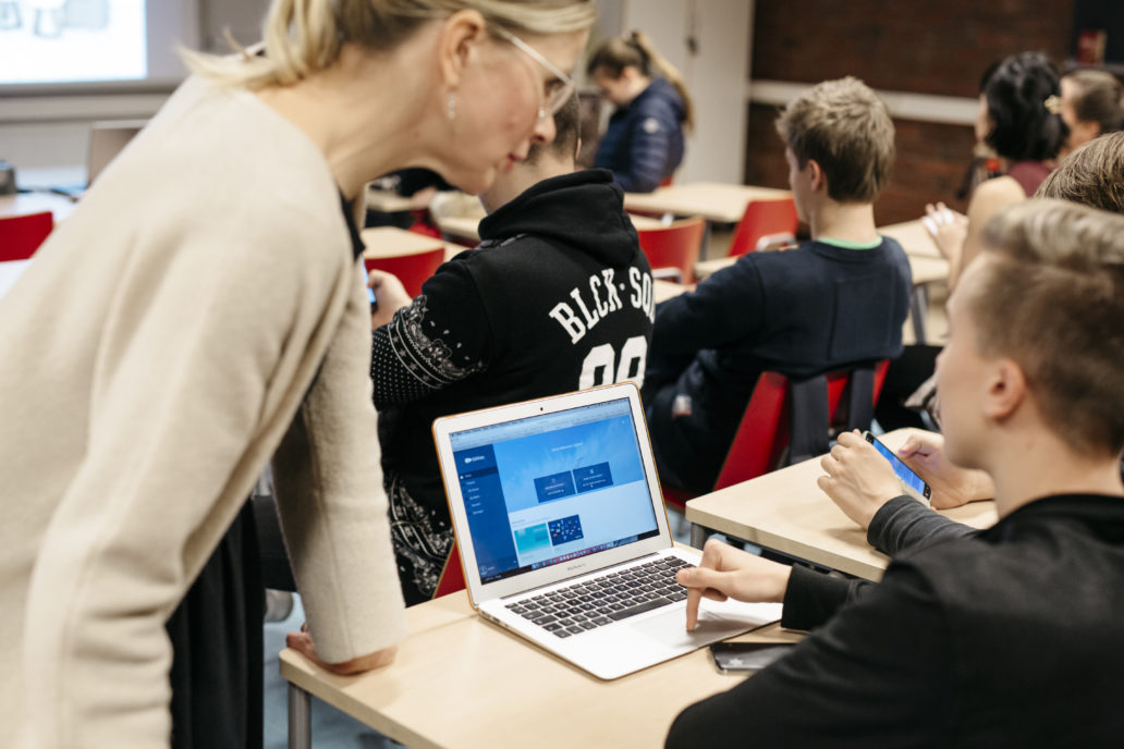 A teacher talking to a boy working on his computer at classroom.