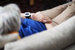 An older woman on couch with smart watch receiving data through wire attached to finger