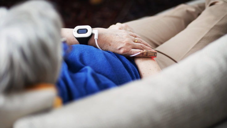 An older woman on couch with smart watch receiving data through wire attached to finger