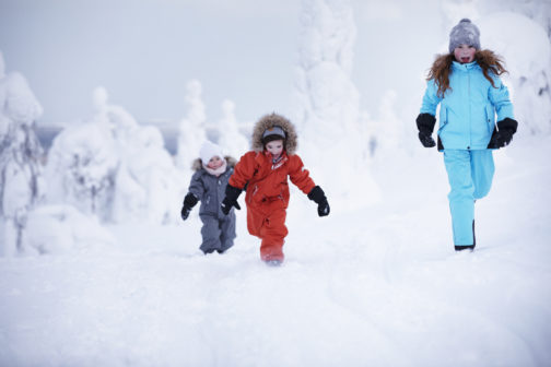 Three children of different ages running in thick winter wear in a snow-covered landscape