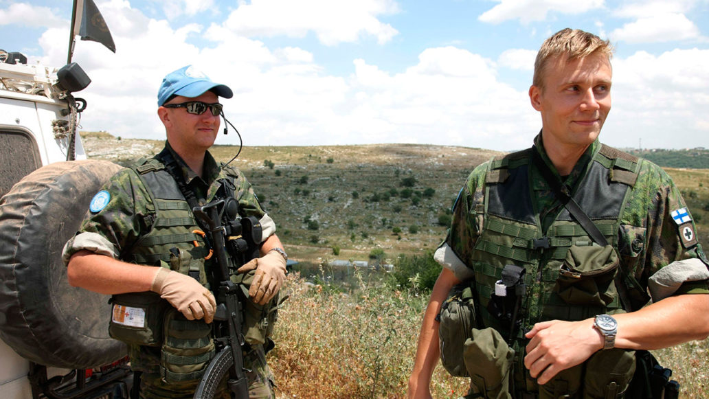 Two men dressed in full army gear standing behind a Jeep. 