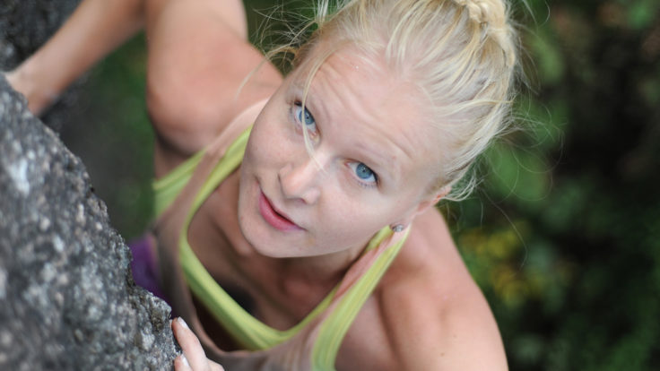 A determined-looking woman facing up while rock climbing.