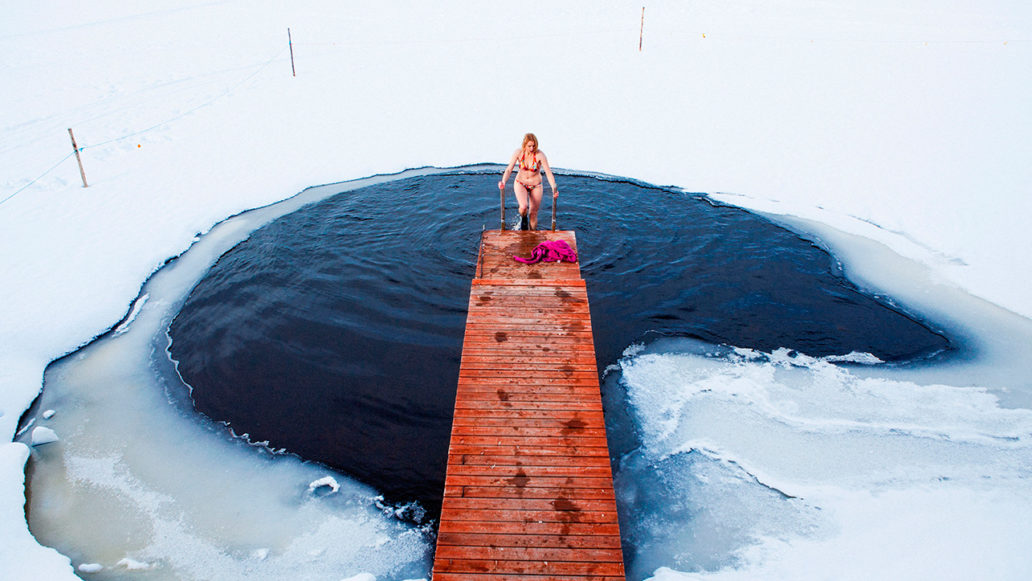 A woman in bikinis climbing on a pier after a swim in a hole in the ice. 