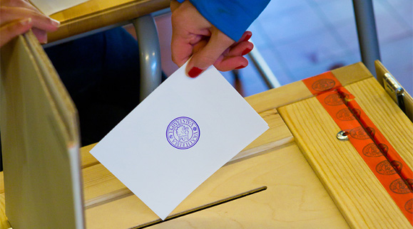 A person putting their voting ballot in a ballot box. 