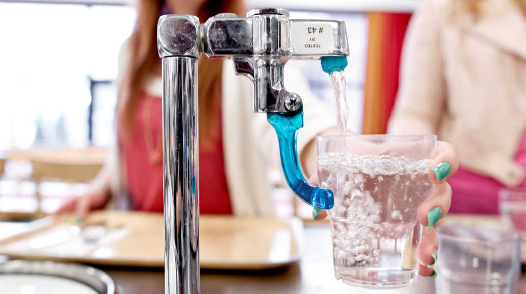 A close-up of a water tap in a restaurant with a person filling their glass from it.